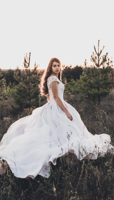 Bride in wedding white dress walking on the meadow in summer at sunset